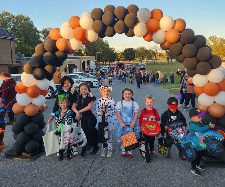 Children posing for a photo under a balloon arch dressed up for halloween